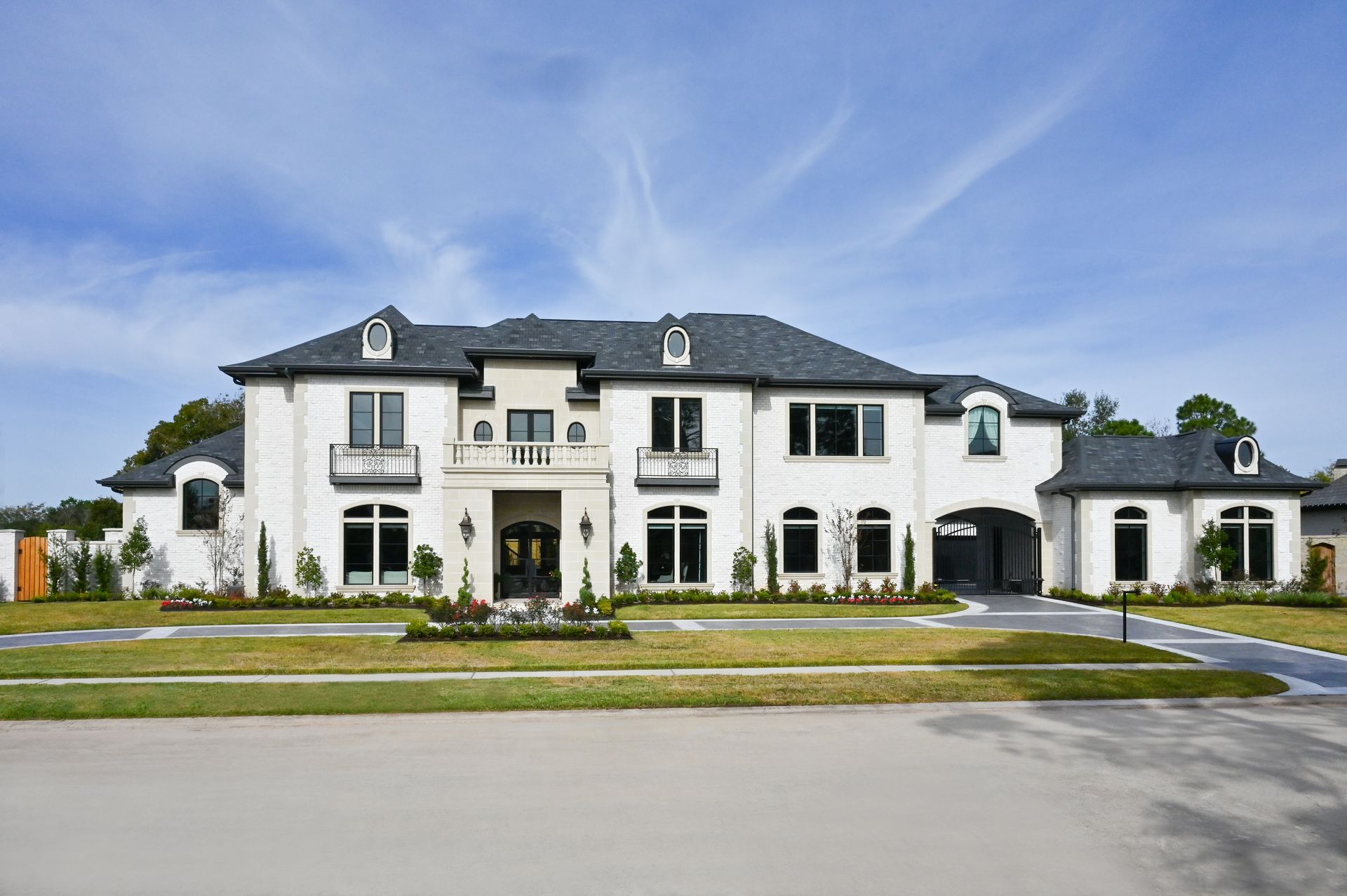 A large white house with a black roof is sitting on top of a lush green lawn.