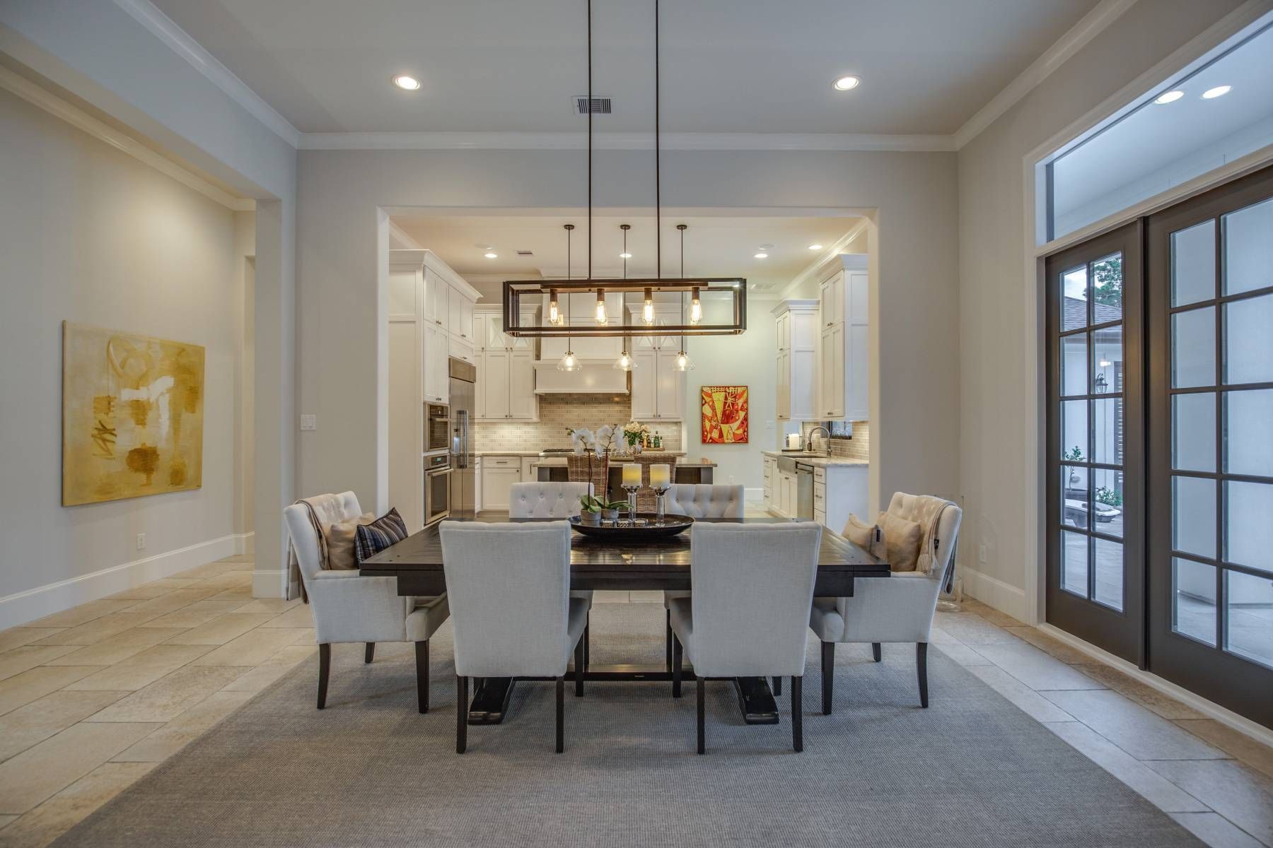A dining room with a table and chairs and a kitchen in the background.