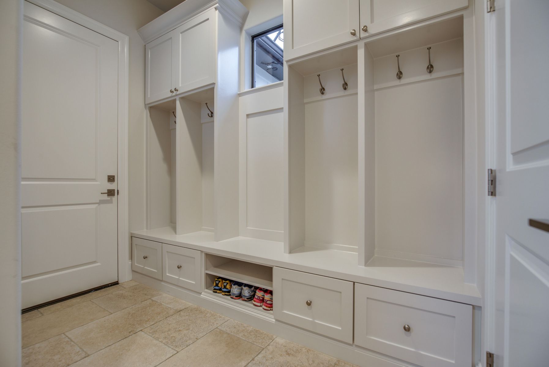 A mud room with white cabinets , drawers , and hooks.