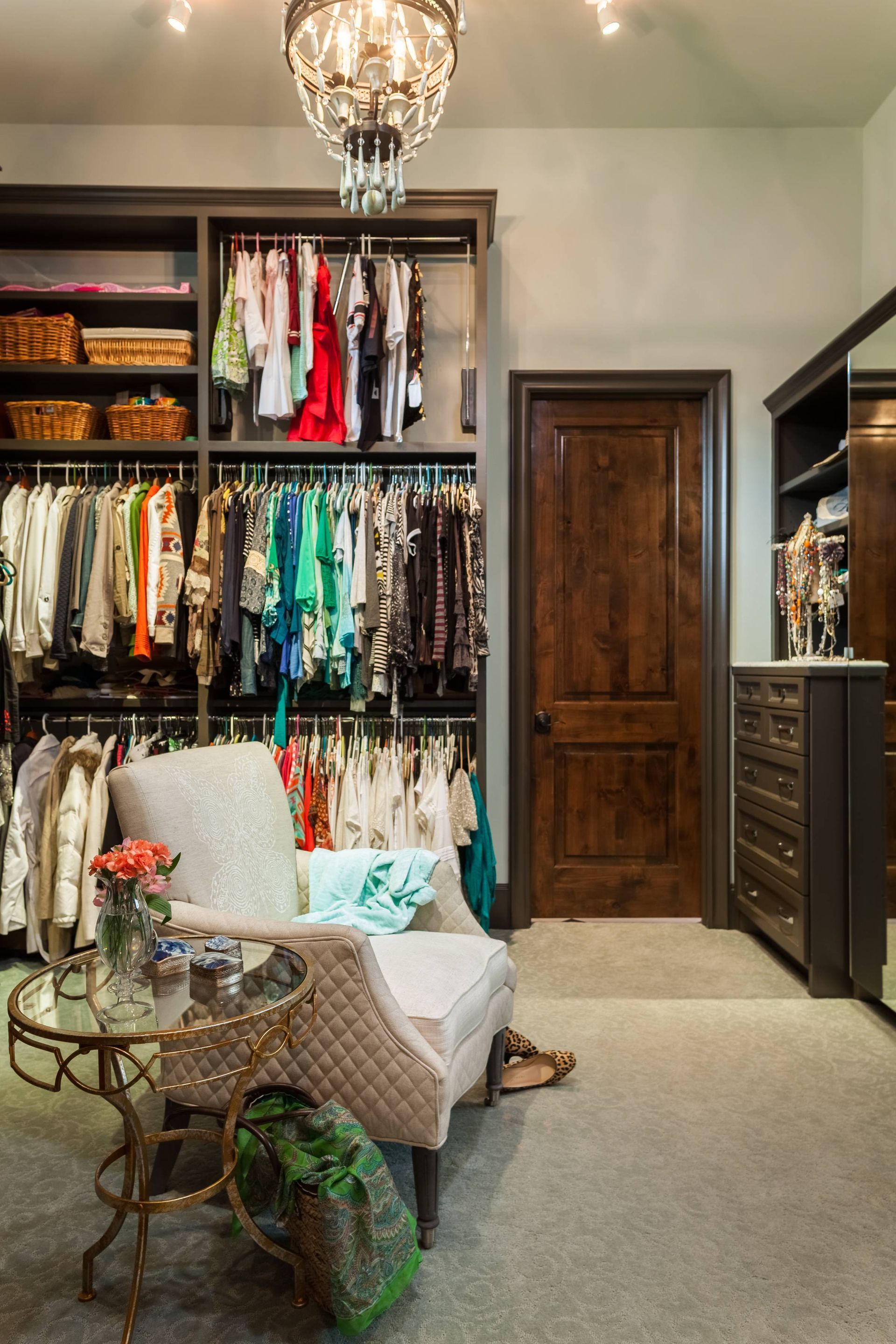 A walk in closet with a chair , table and chandelier.