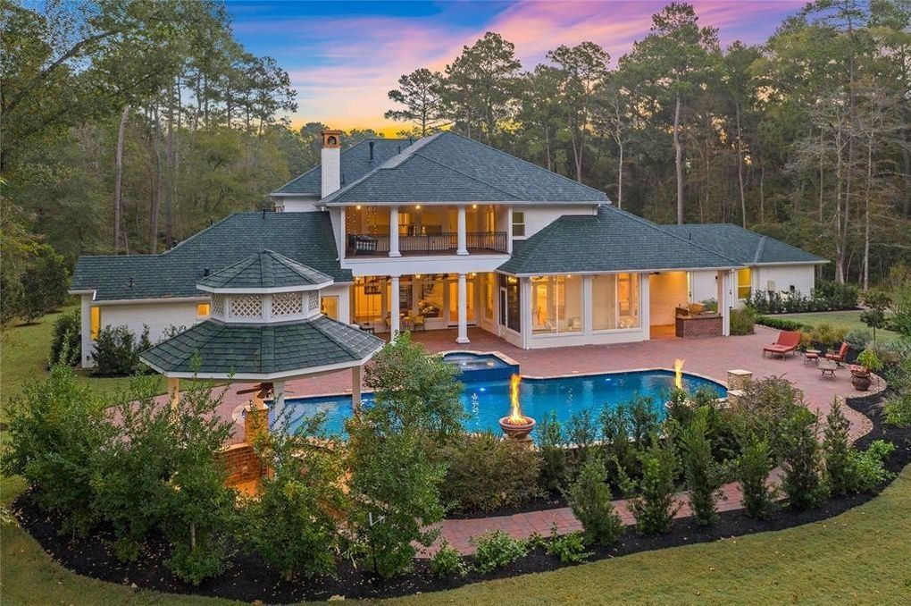 An aerial view of a large house with a large swimming pool surrounded by trees.