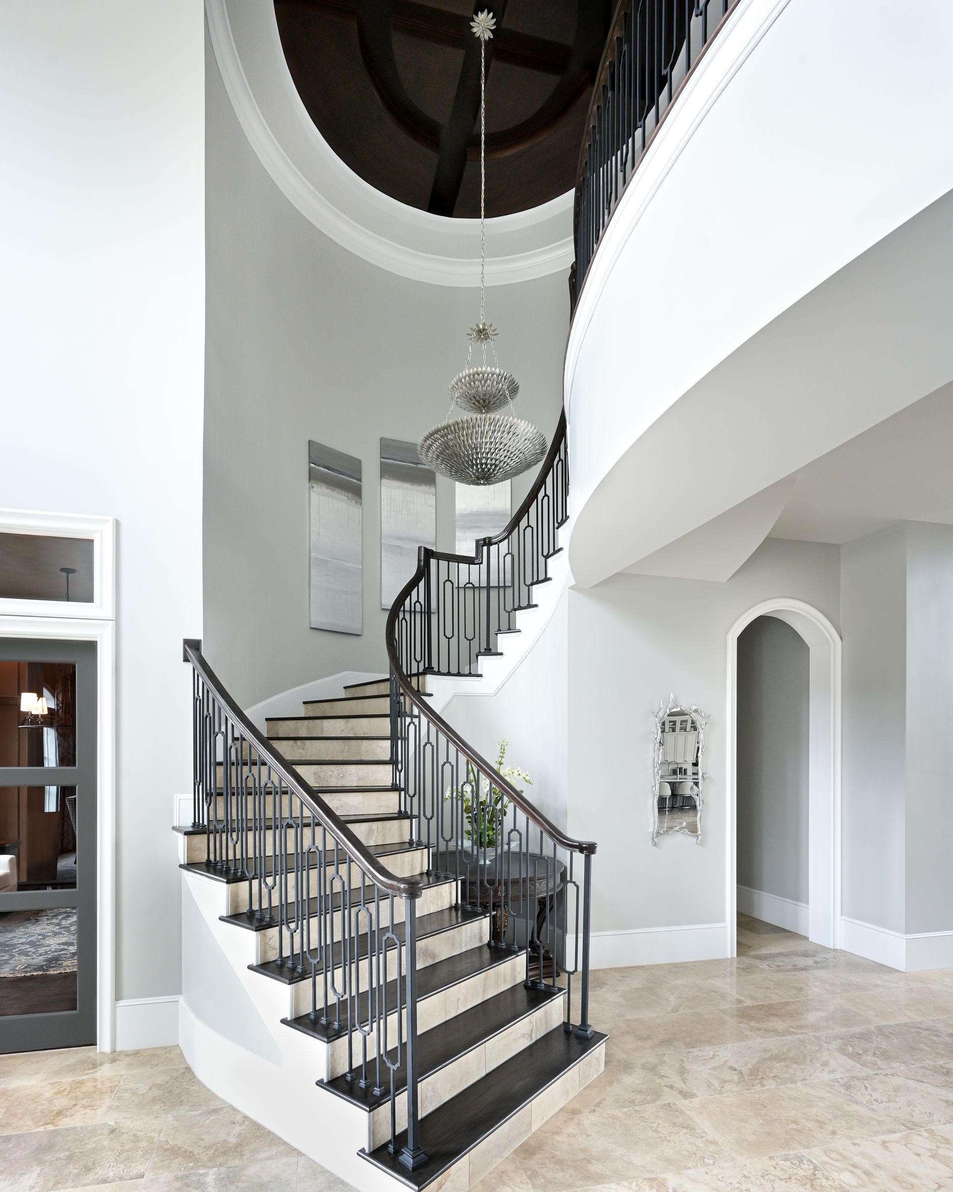 A curved staircase with a black railing and a chandelier hanging from the ceiling