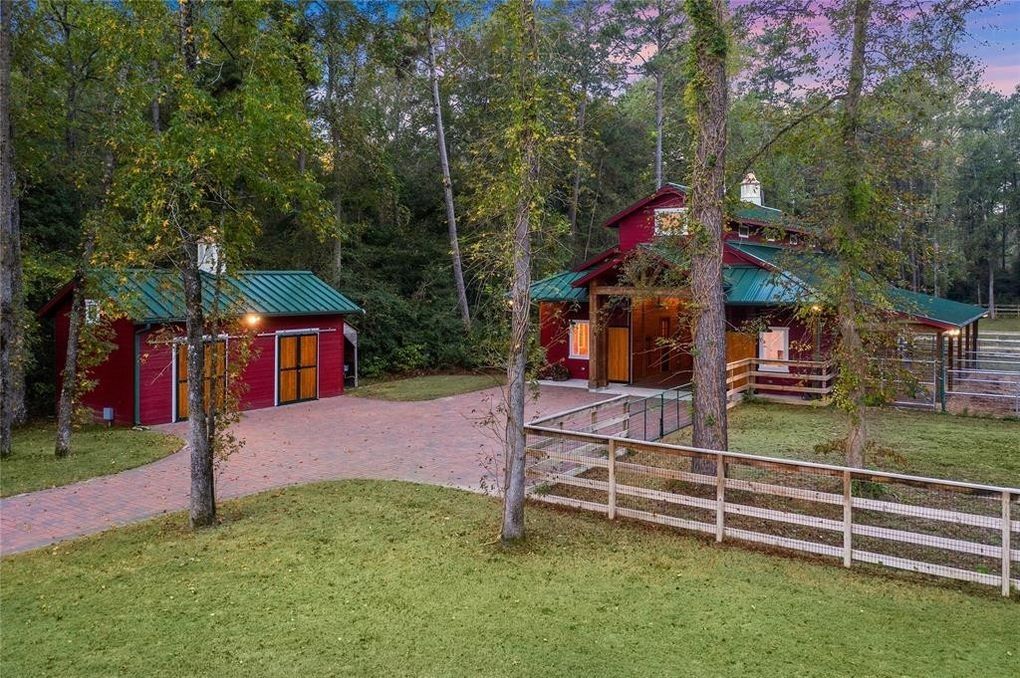 A red barn with a green roof is surrounded by trees and a white fence.