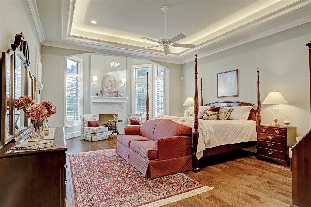 A large bedroom with a four poster bed , couch , dresser and fireplace.
