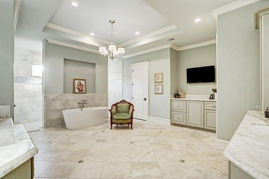A large bathroom with a tub , chair , sink and television.