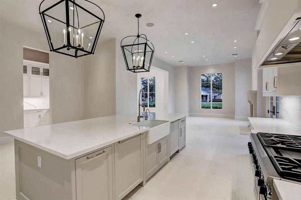 A kitchen with white cabinets , a stove , a sink , and a large island.