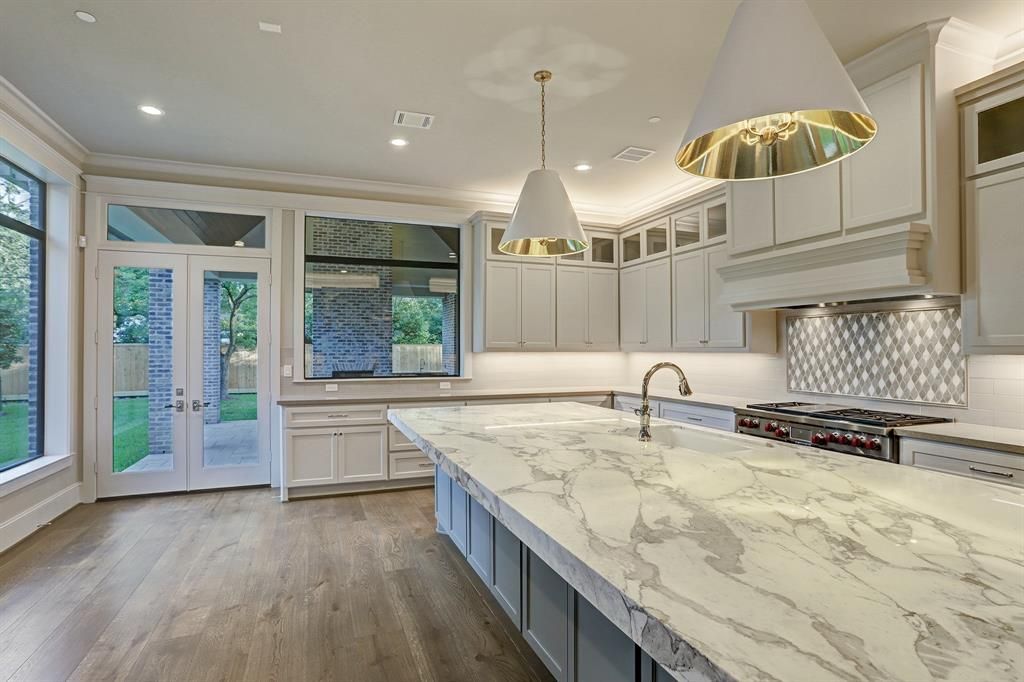 An empty kitchen with a large island and marble counter tops.
