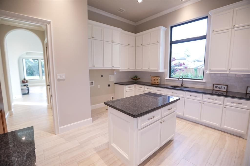 A kitchen with white cabinets , black counter tops , and a large island.