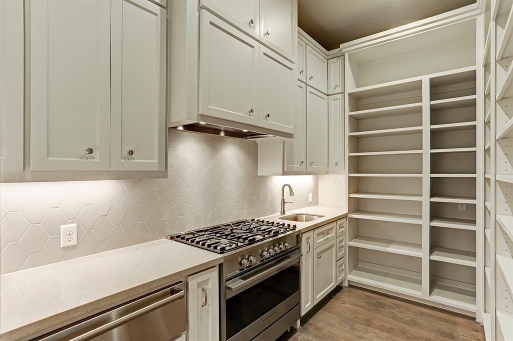 A kitchen with a stove , oven , sink , and shelves.