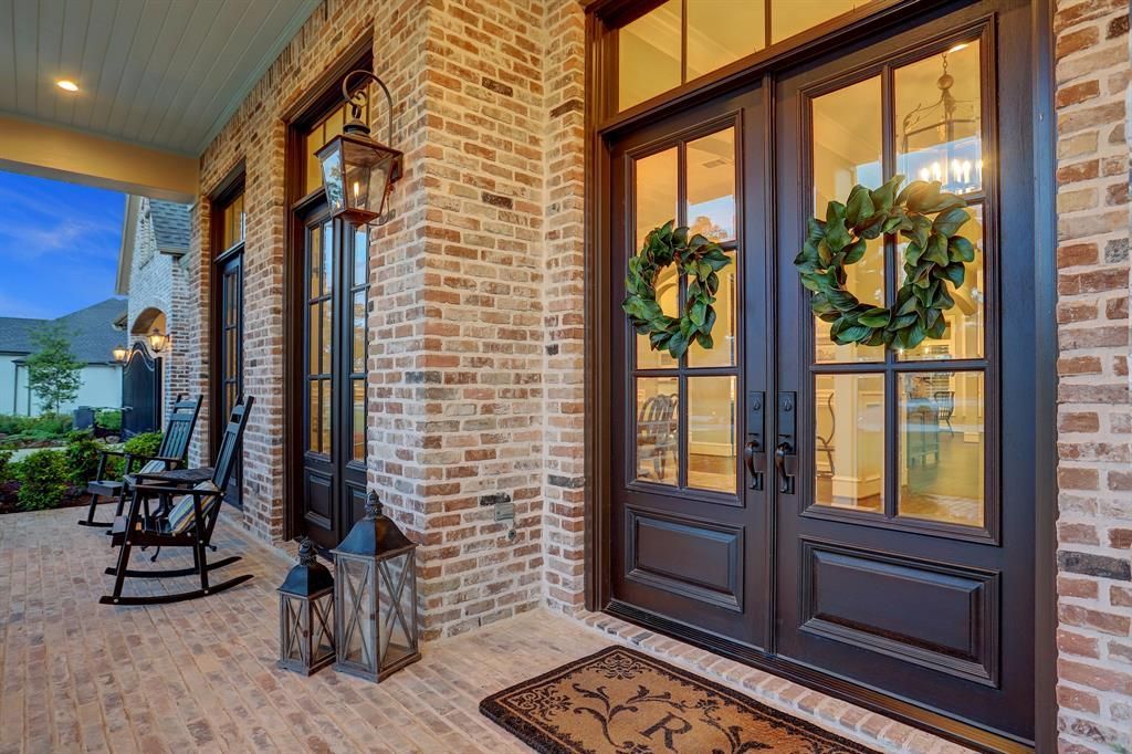 The front porch of a brick house with rocking chairs and lanterns.