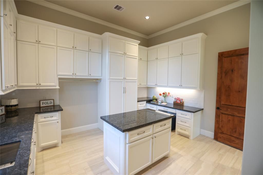 A kitchen with white cabinets , granite counter tops , and a large island.