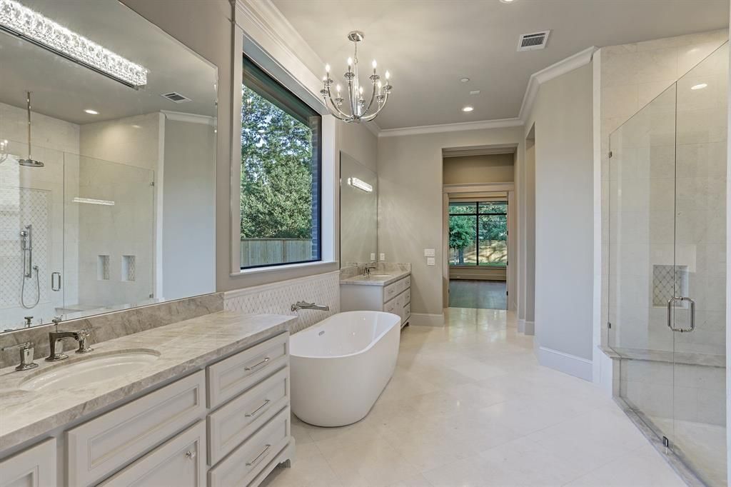 A bathroom with a tub , sinks , mirrors and a chandelier.