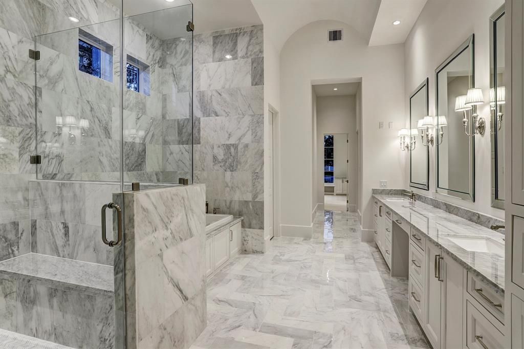 A large bathroom with marble tiles , a walk in shower , two sinks , and two mirrors.