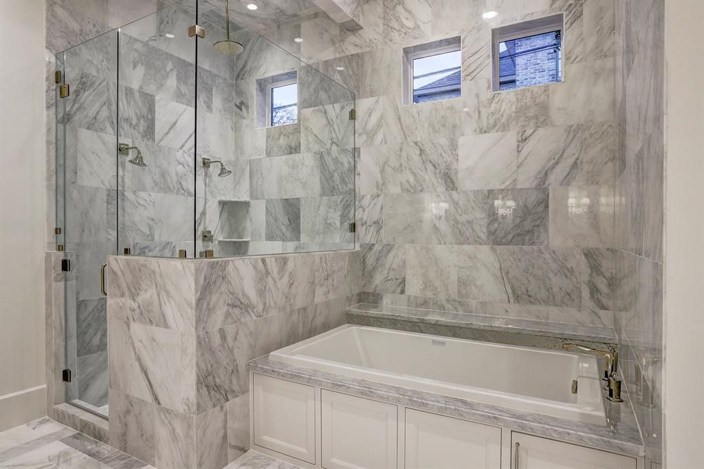 A bathroom with marble tiles , a tub and a walk in shower.
