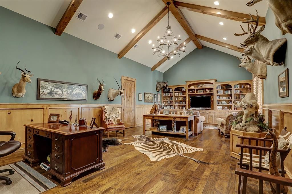 A living room with a desk , chairs , and a deer head on the wall.