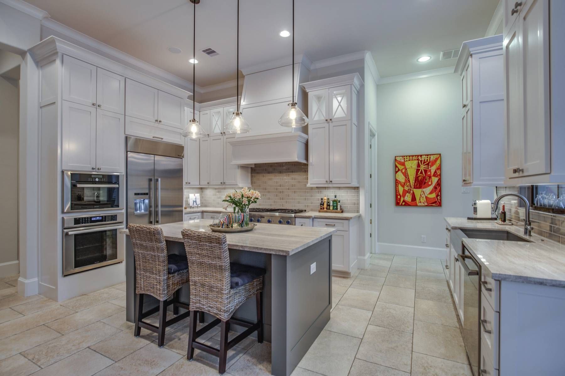 A kitchen with white cabinets , stainless steel appliances , a large island , and a painting on the wall.