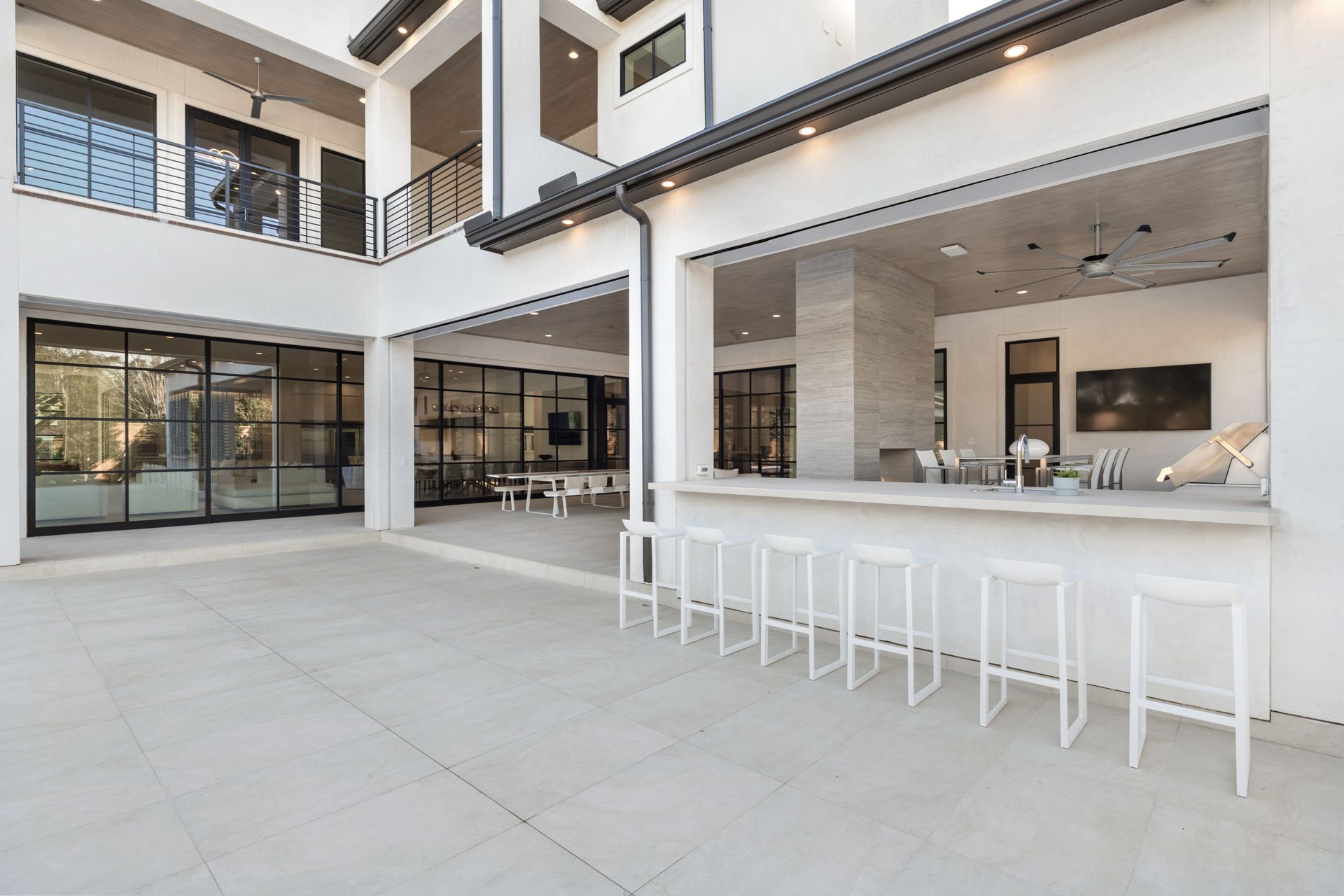 A large white house with a bar and stools in the backyard.