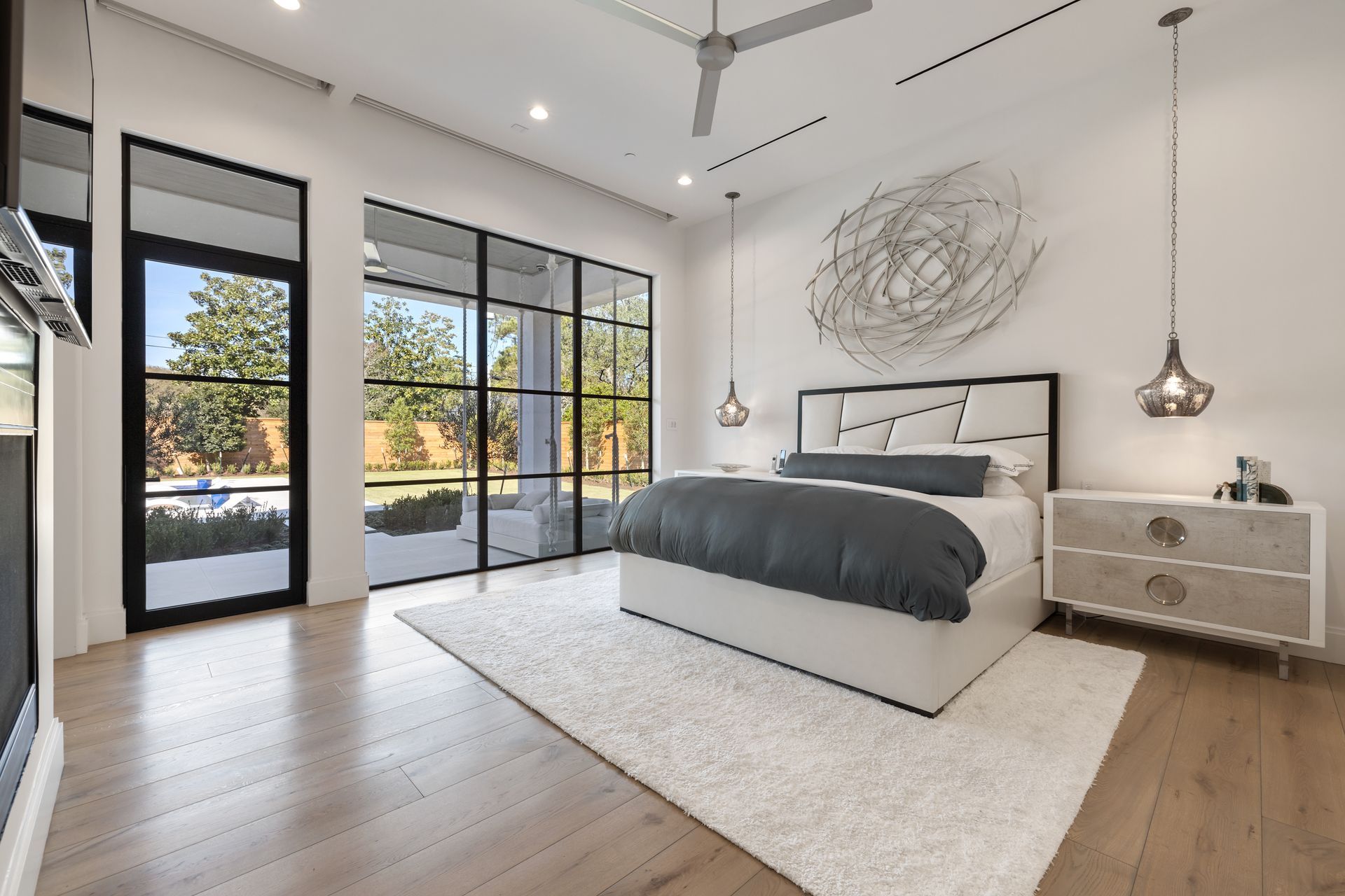 A bedroom with a bed , nightstand , dresser , and large windows.