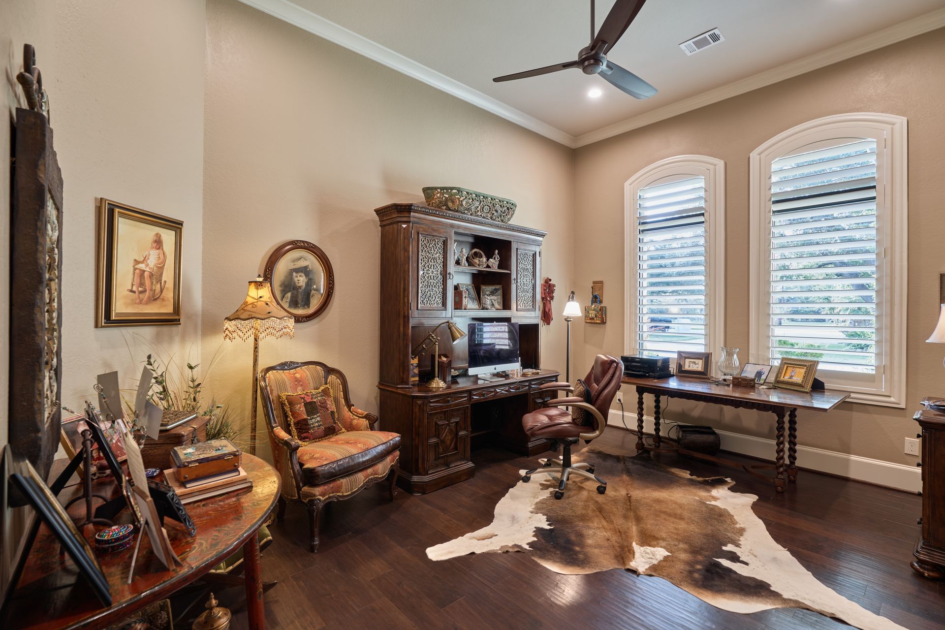 A home office with a cowhide rug on the floor and a ceiling fan.