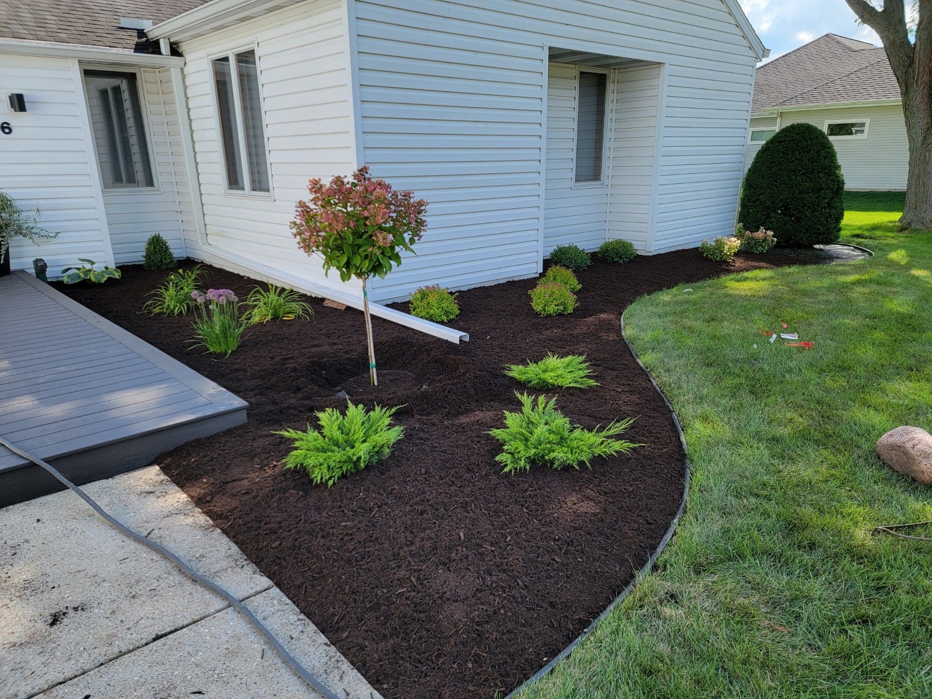 A white house with a lush green yard, new landscaping, and water runoff 