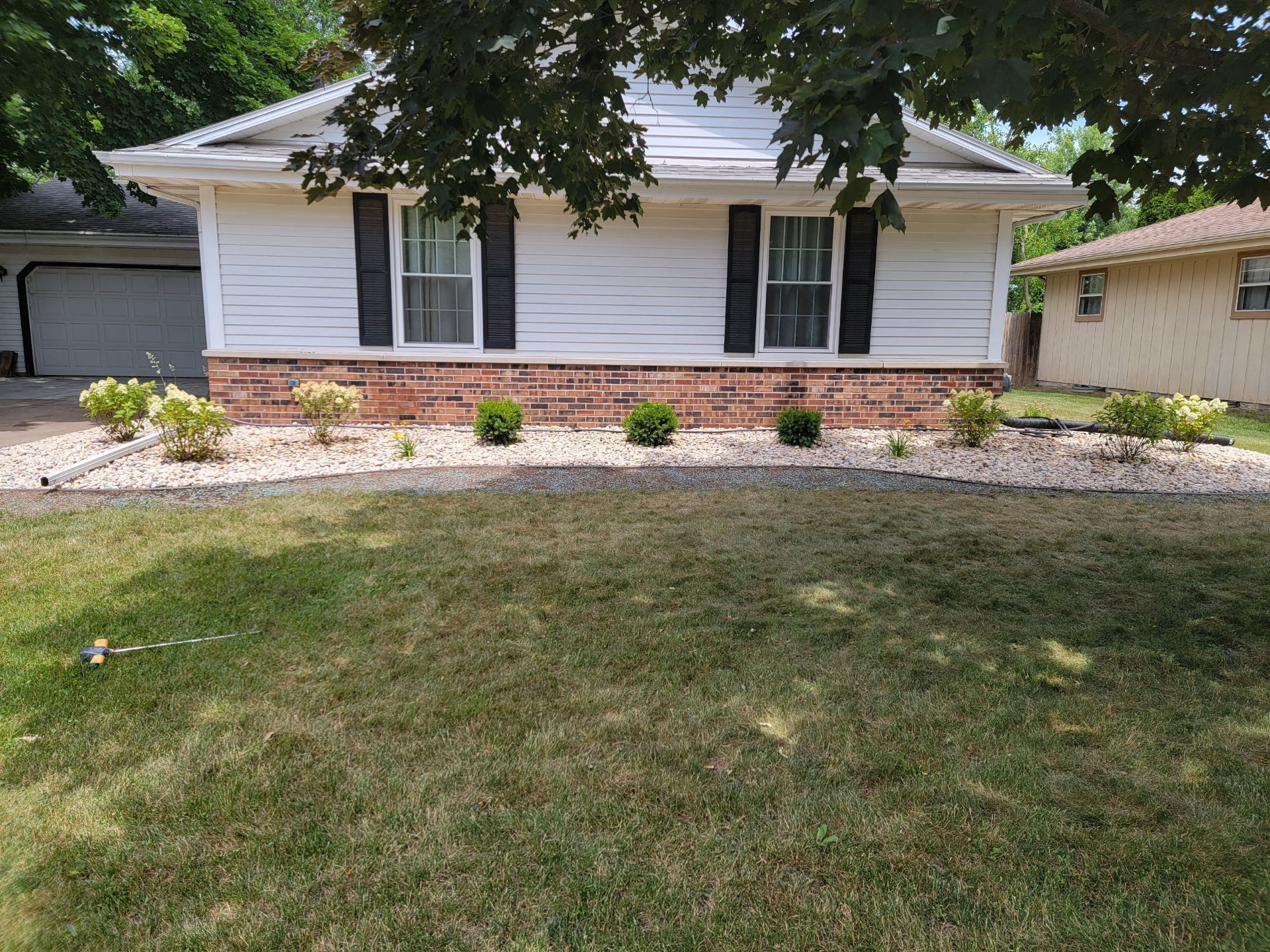A white house with a brick wall and black shutters is sitting on top of a lush green lawn.