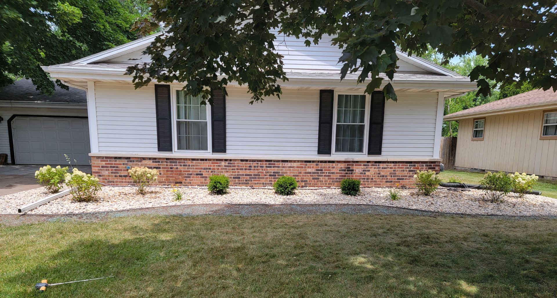 A white house with black shutters and new landscaping and gravel