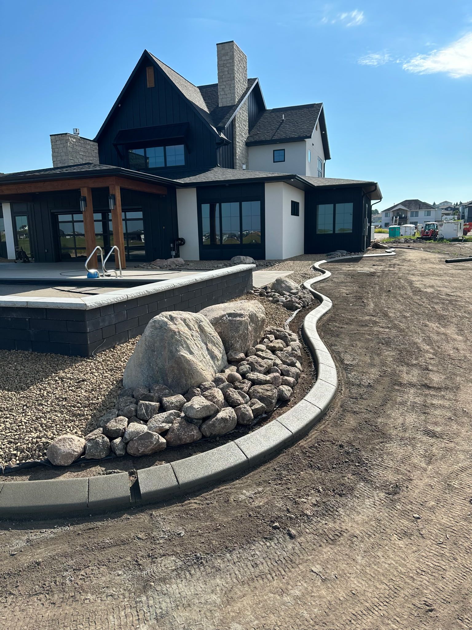 Modern house with dark siding and a stone wall bordering a rock garden.