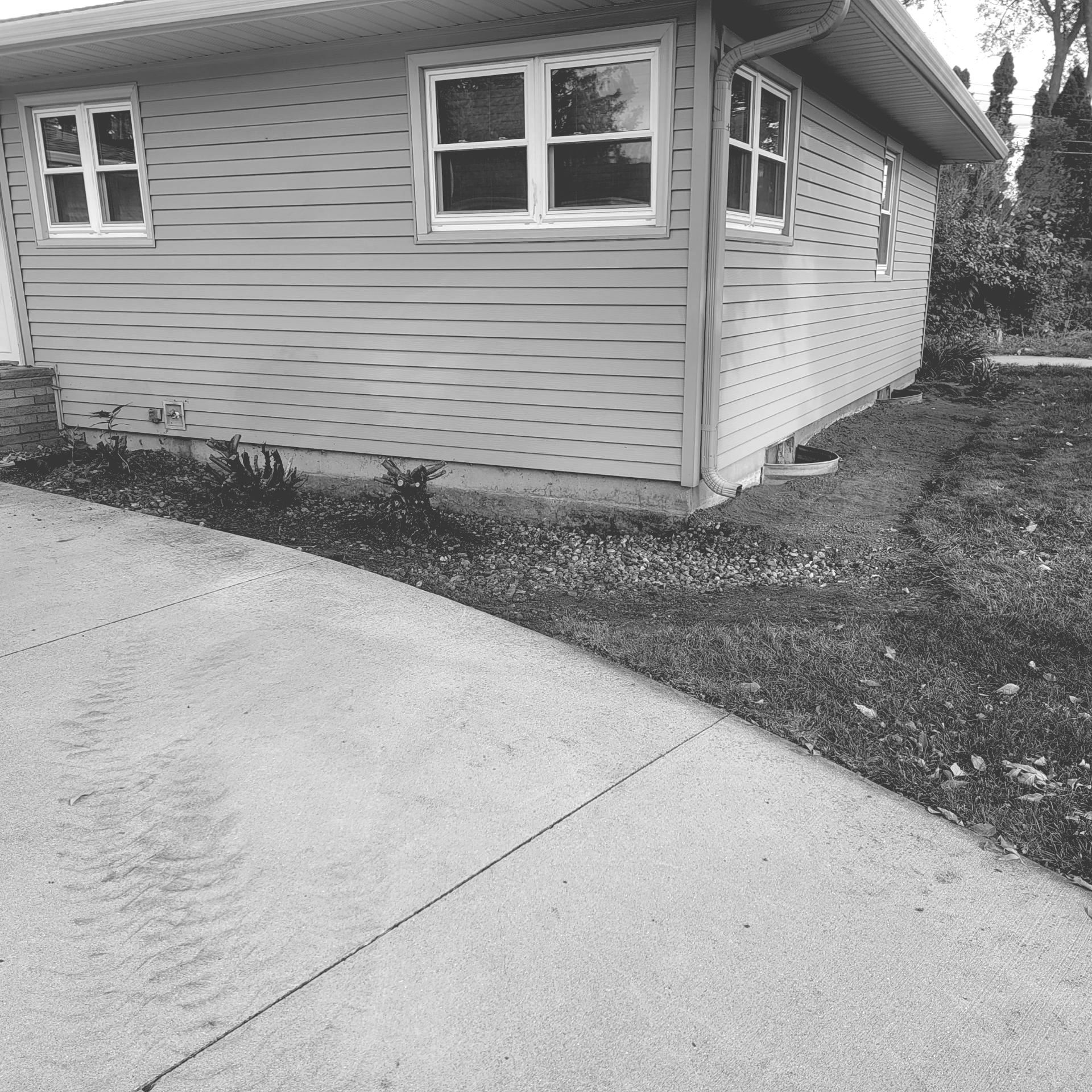 A black and white photo of a house with a driveway in front of it