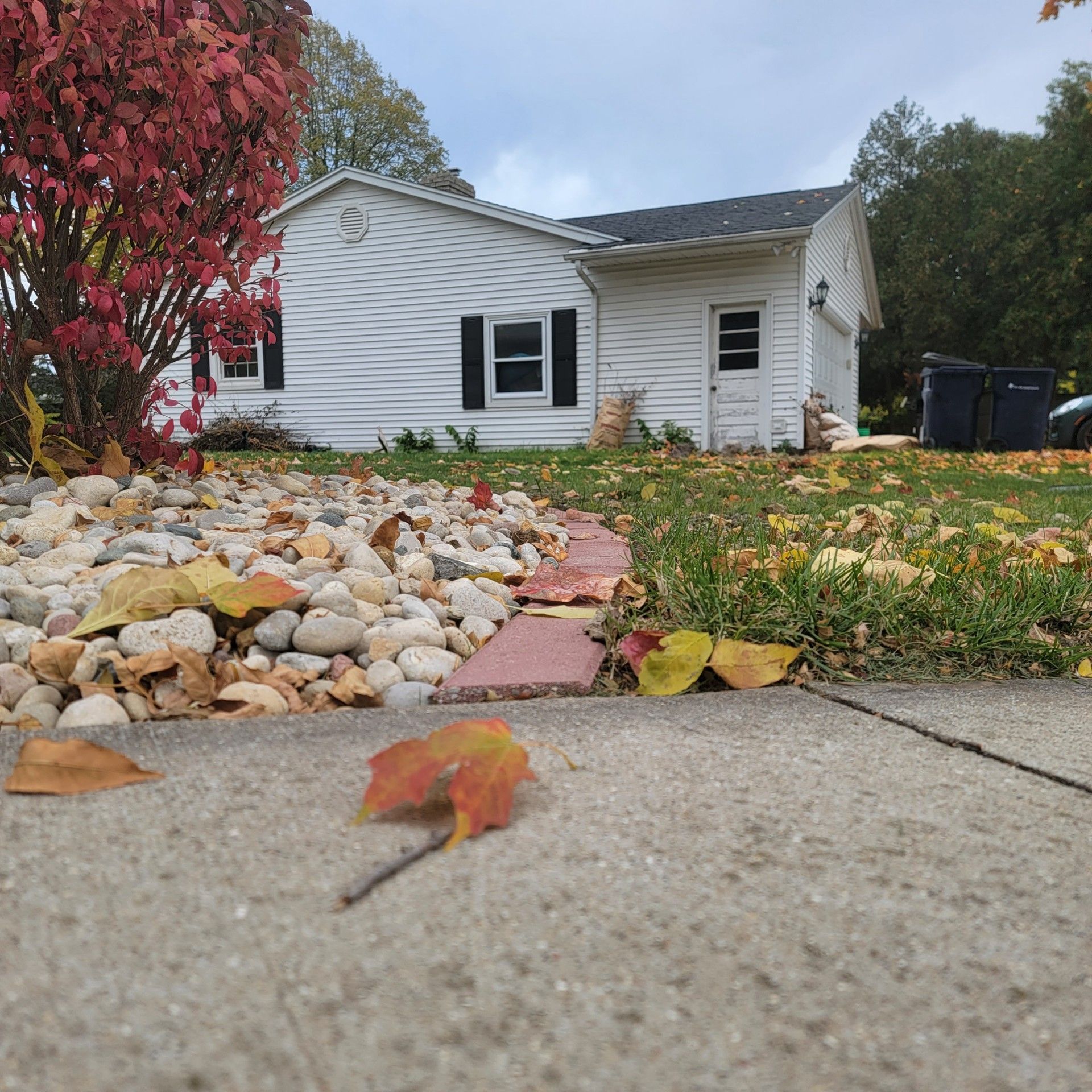 A white house with black shutters is surrounded by rocks garden and edging