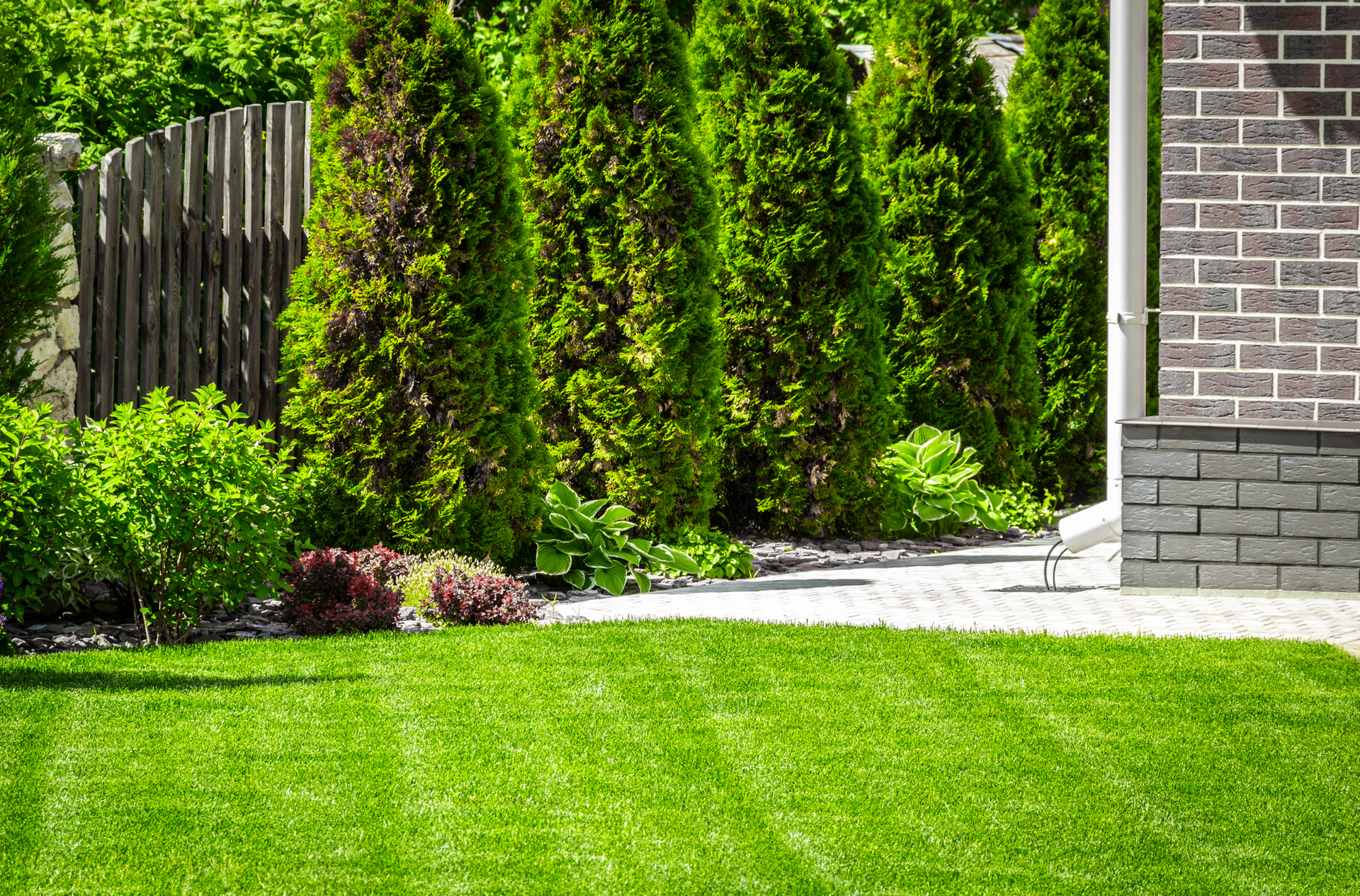 A lush green lawn in front of a brick house with trees and bushes.