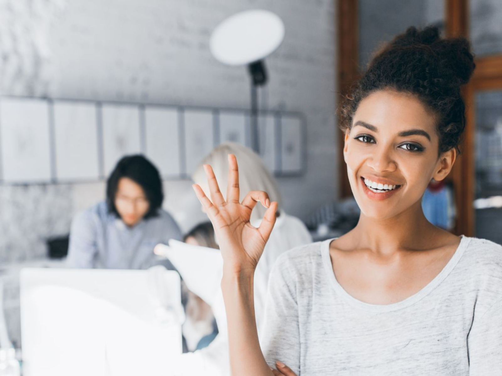 Woman giving the okay sign in front of people working in the pacground