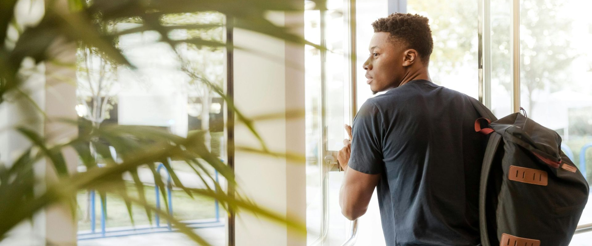 Student with backpack walking thorough a glass door of a building