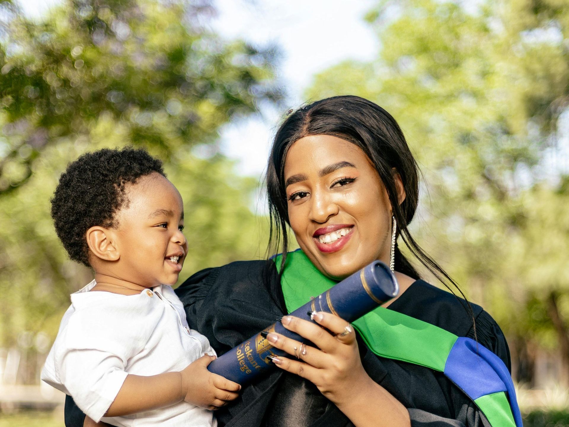 Woman in a college graduation gown with a young child on her hip 