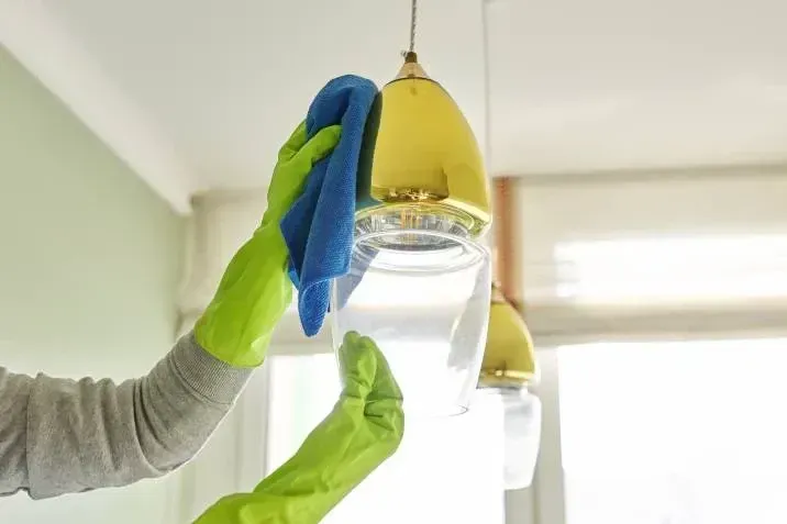 A person wearing green gloves is cleaning a light fixture with a cloth.