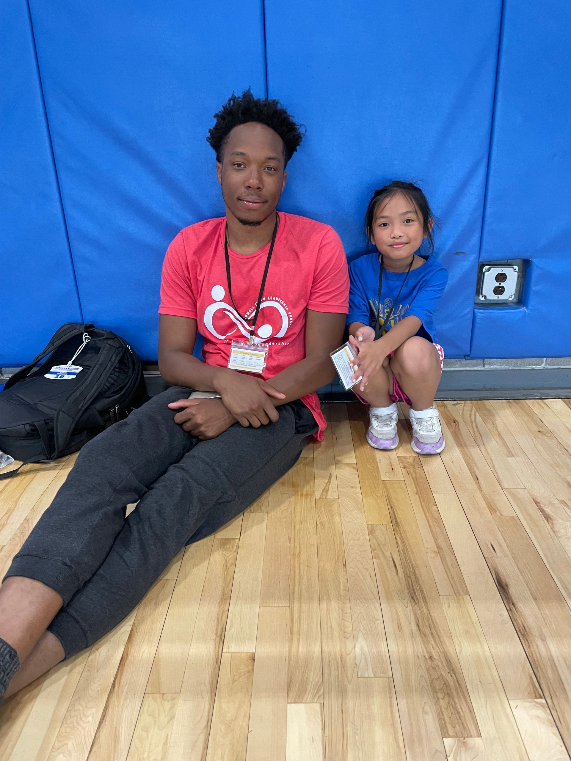 A man and a little girl are sitting on the floor in a gym.