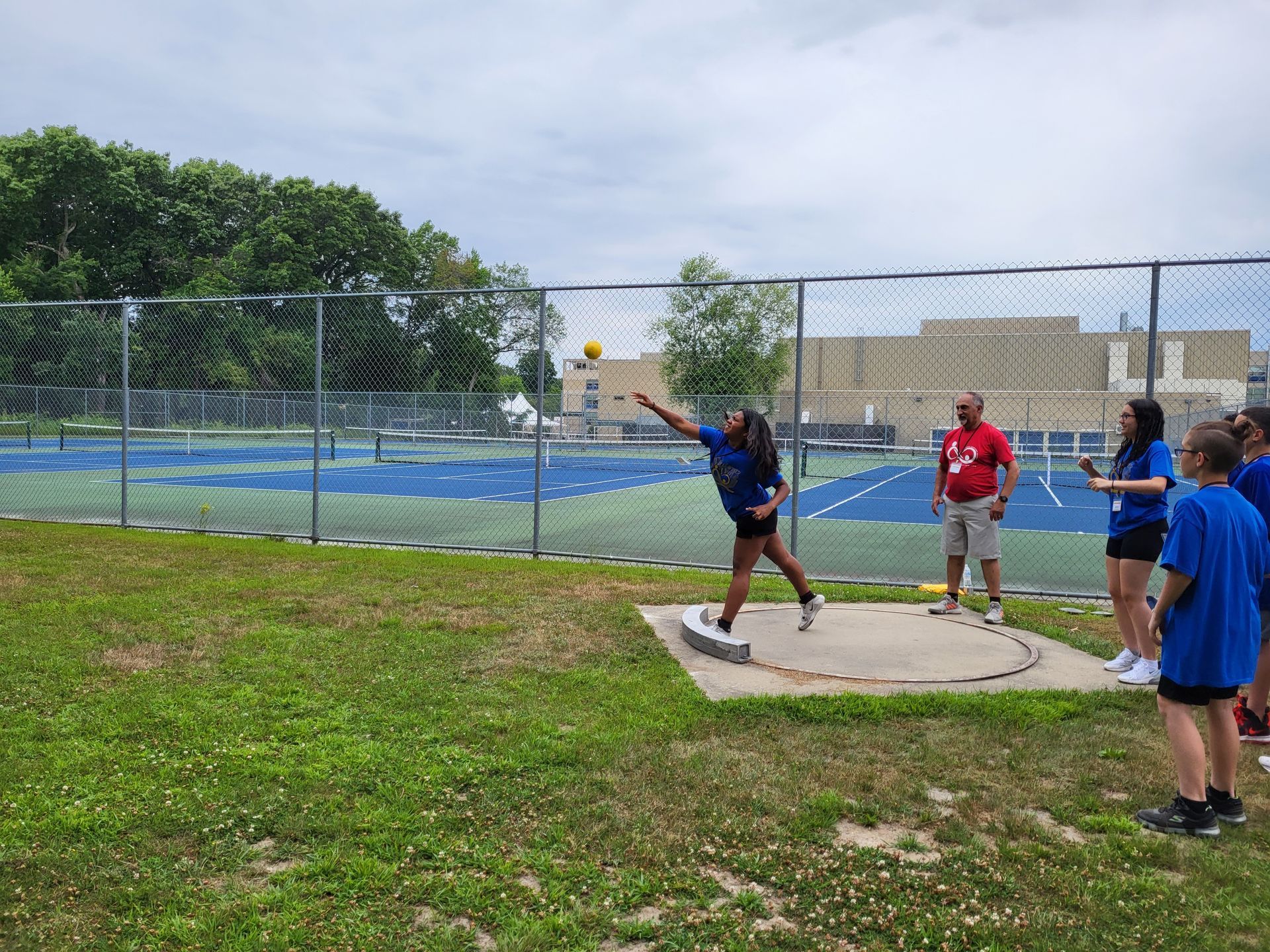 A woman is throwing a ball in a field while a group of people watch.