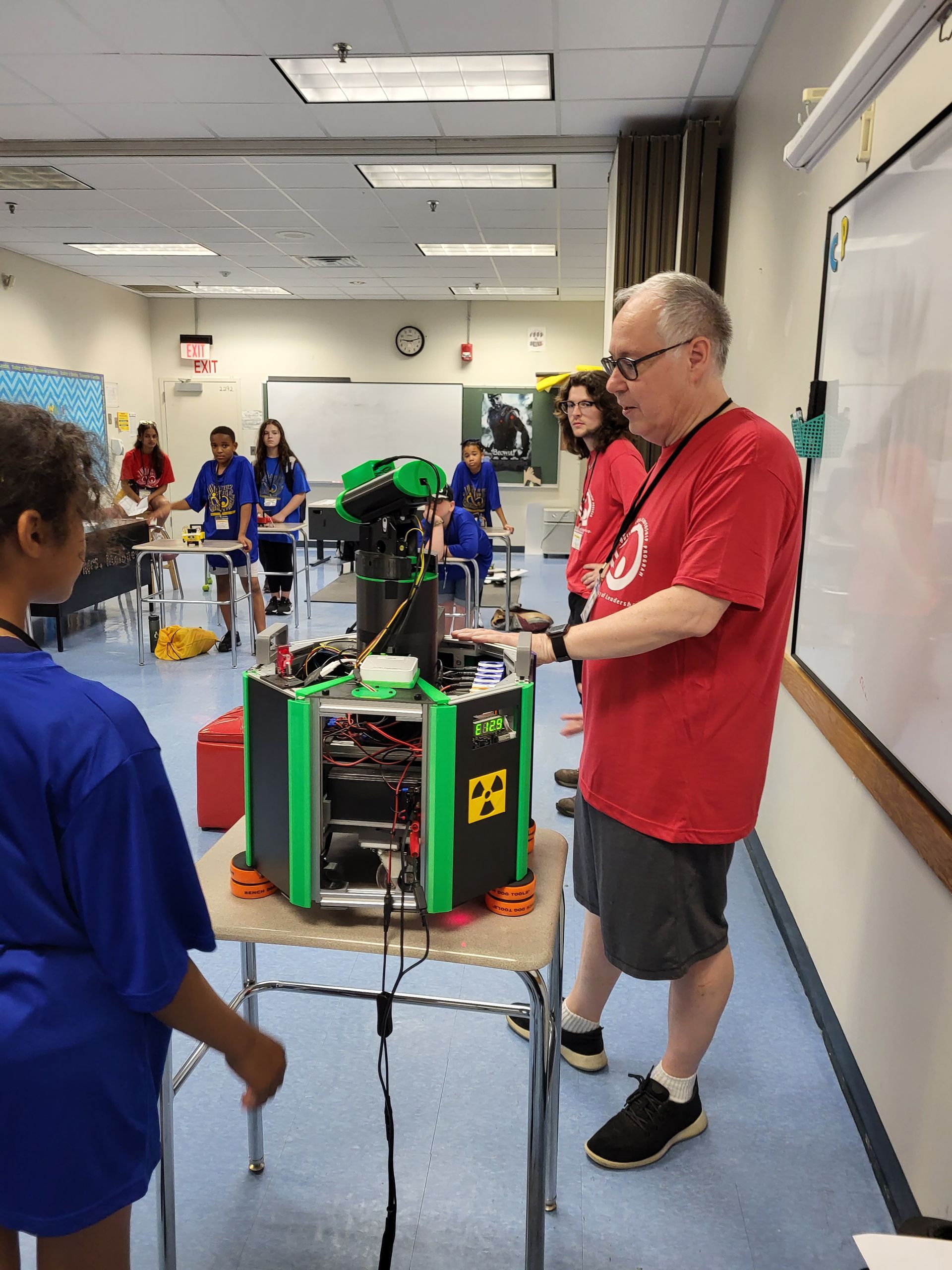 A man in a red shirt is standing next to a table with a green box on it.