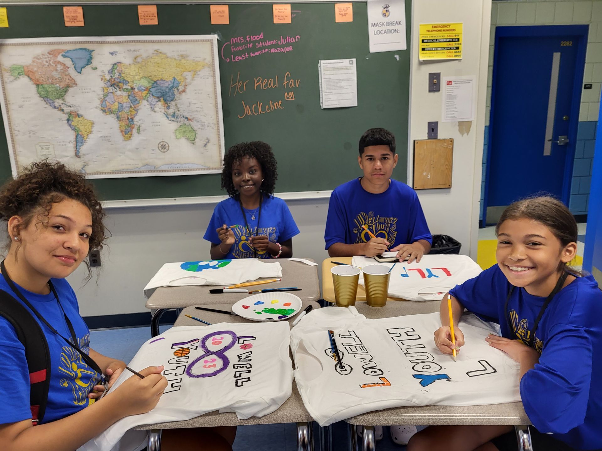 A group of children are sitting at a table painting t-shirts.