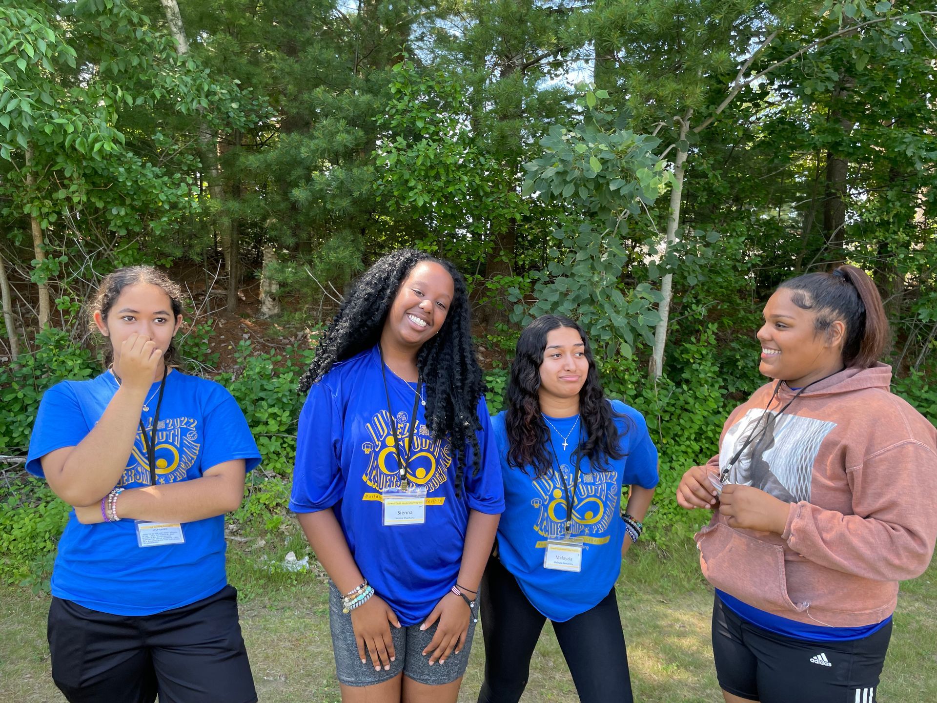 A group of young women are standing next to each other in front of trees.