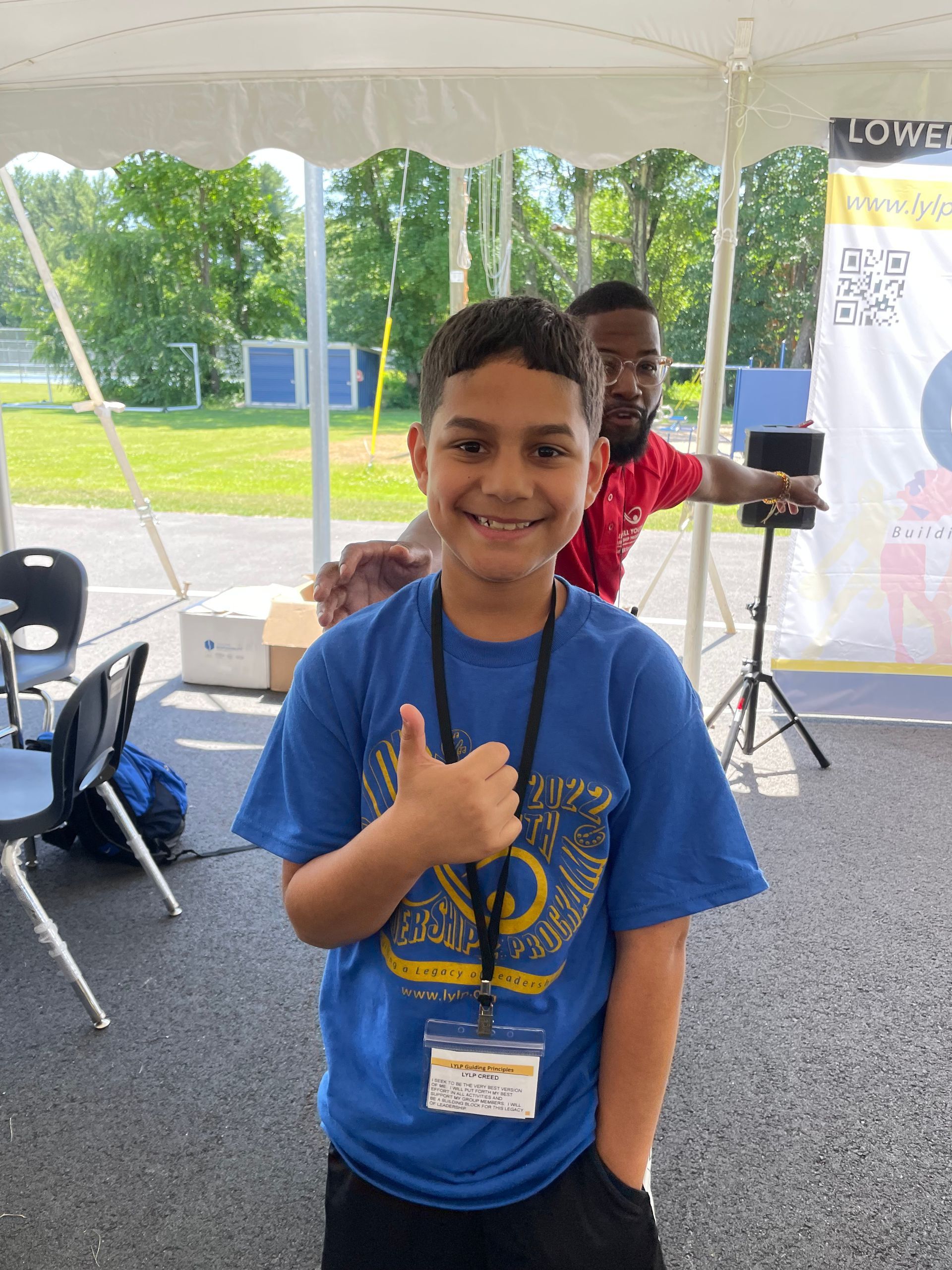 A young boy in a blue shirt is giving a thumbs up.