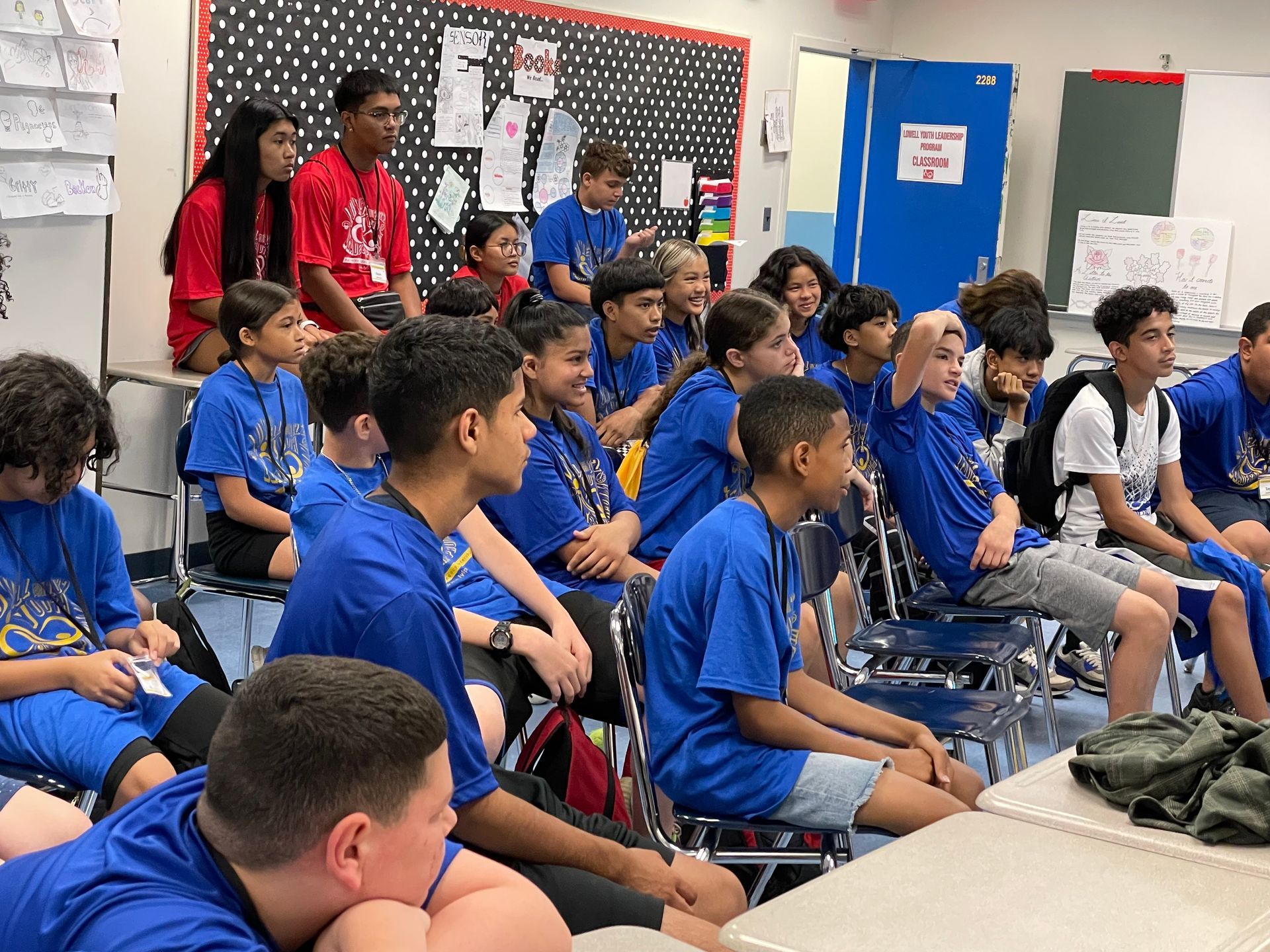 A group of young people in blue shirts are sitting in a classroom.