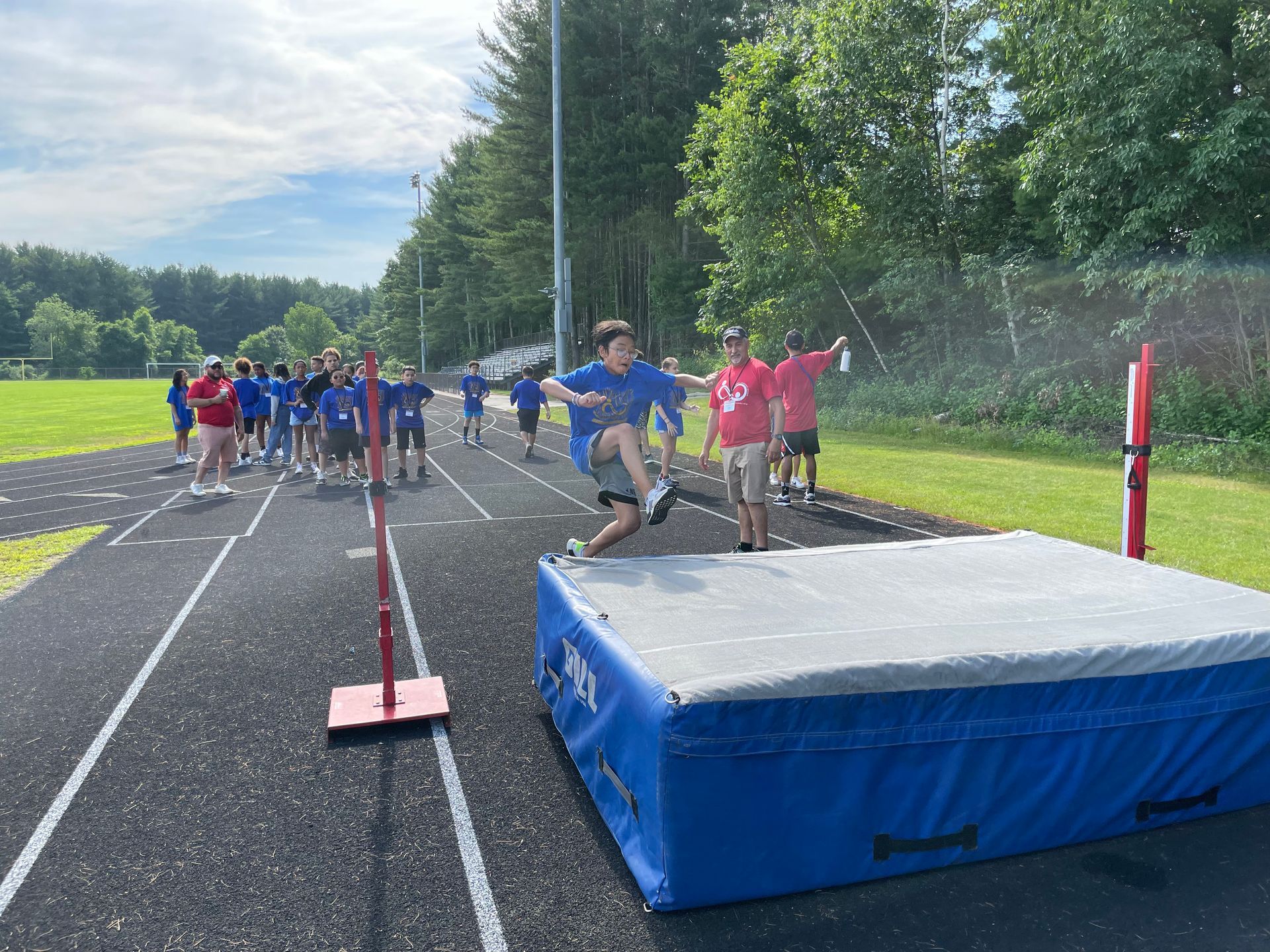 A group of children are jumping over a high jump mat on a track.