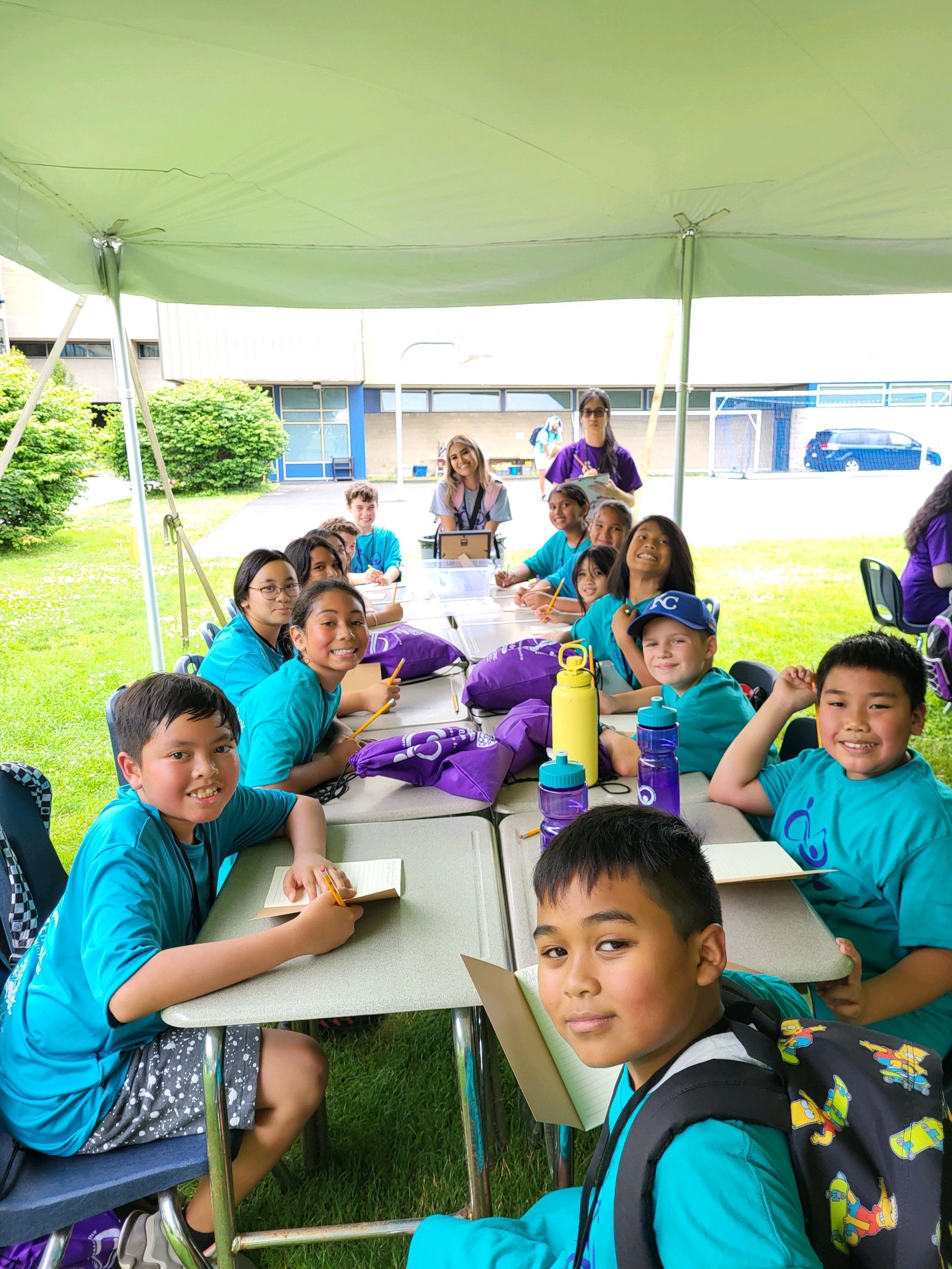 A group of children are sitting at tables under a tent.