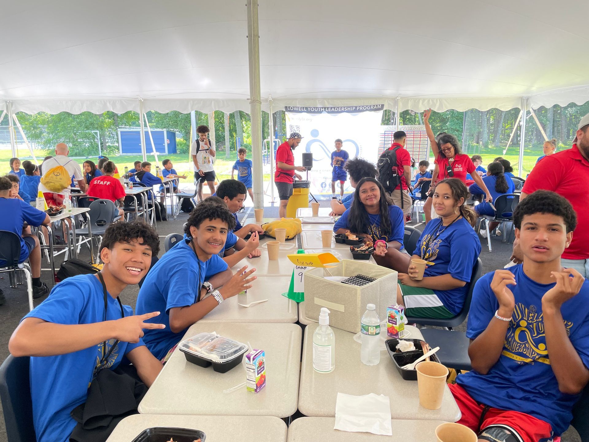 A group of people are sitting at tables under a tent eating food.