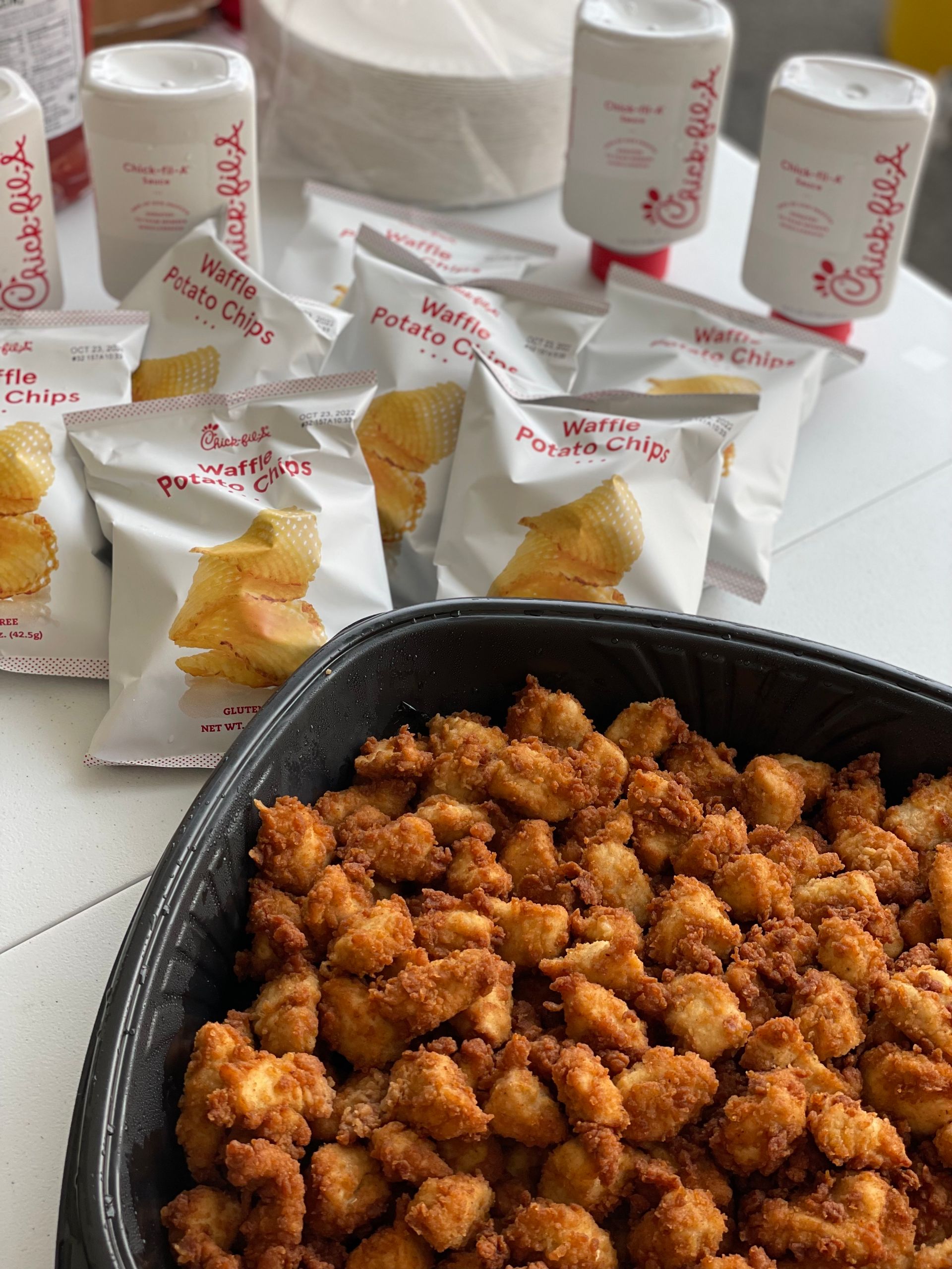 A bowl of fried chicken and potato chips on a table.