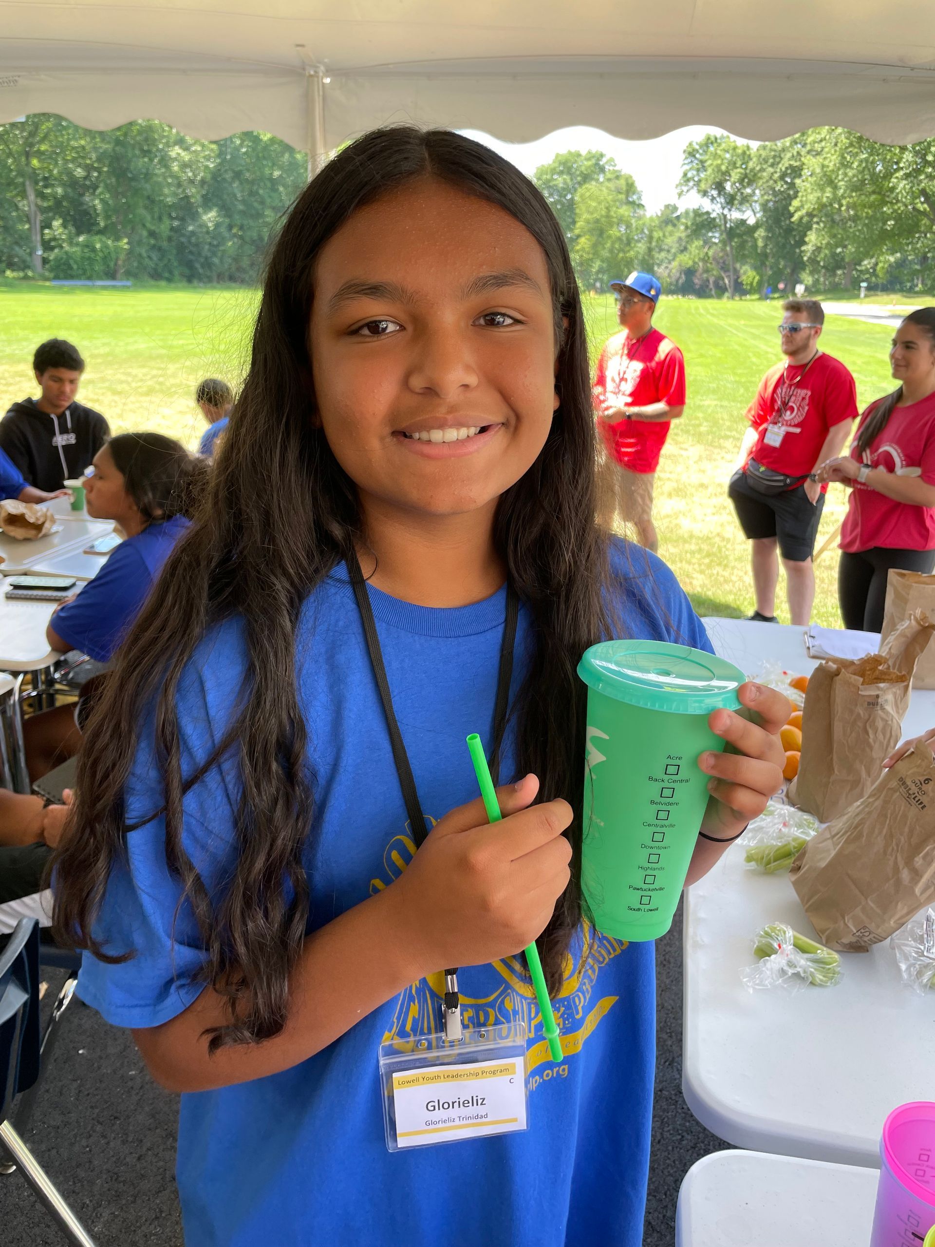 A young girl in a blue shirt is holding a green cup with a straw.