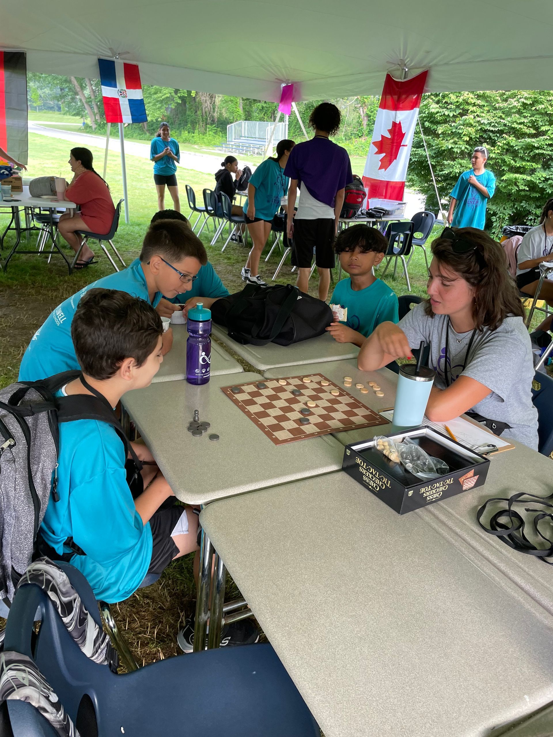 A group of people are sitting at tables under a tent playing chess.