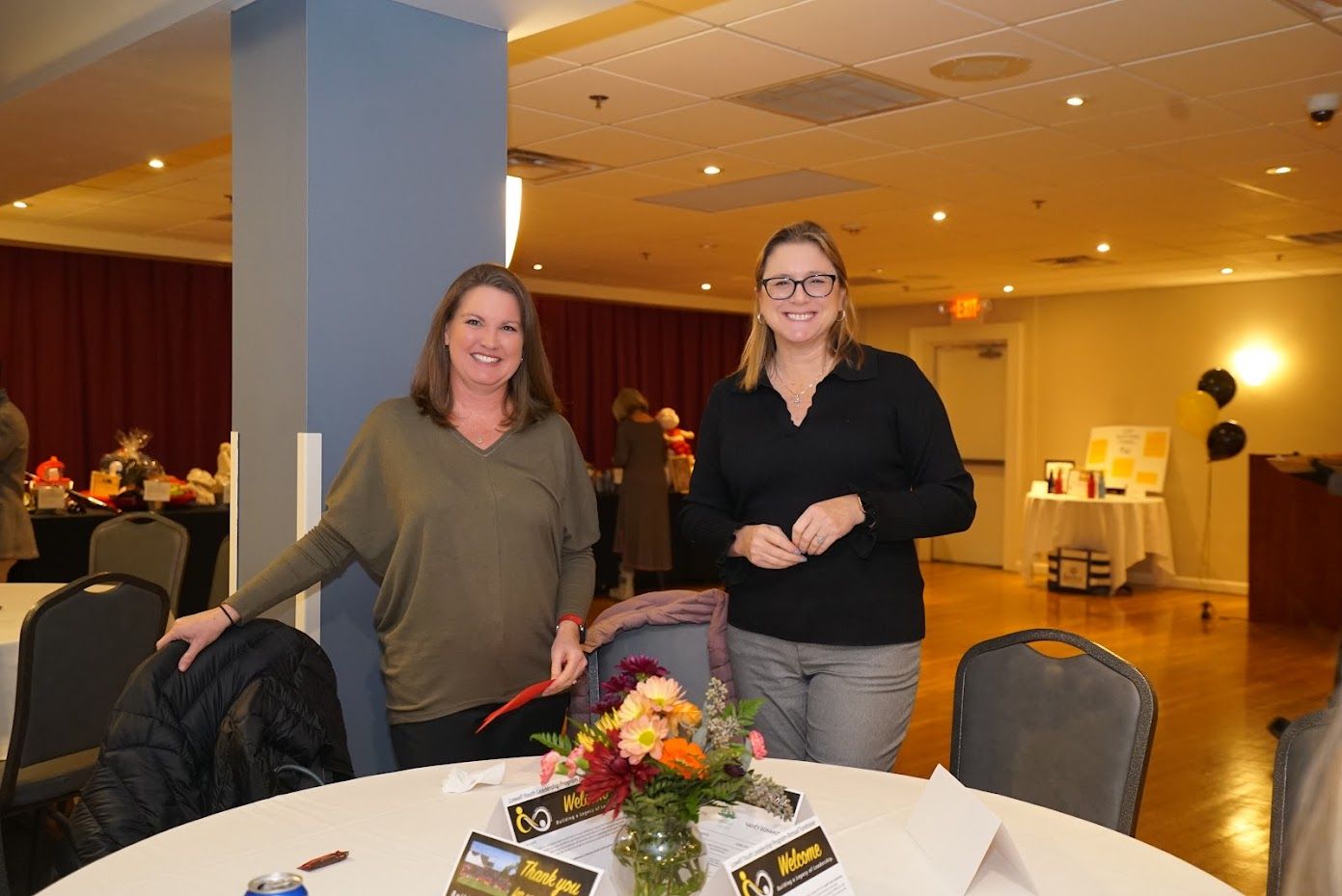 Two women are standing next to a table with flowers on it.