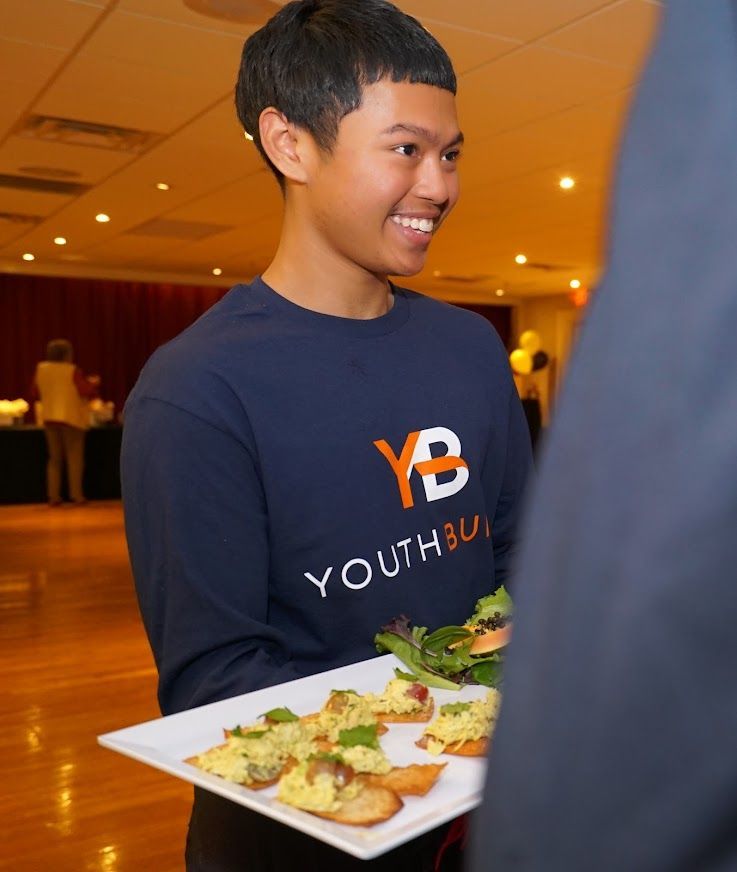 A young man wearing a youthful shirt is holding a plate of food