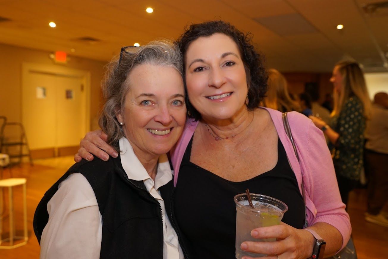 Two women are posing for a picture and one is holding a drink.